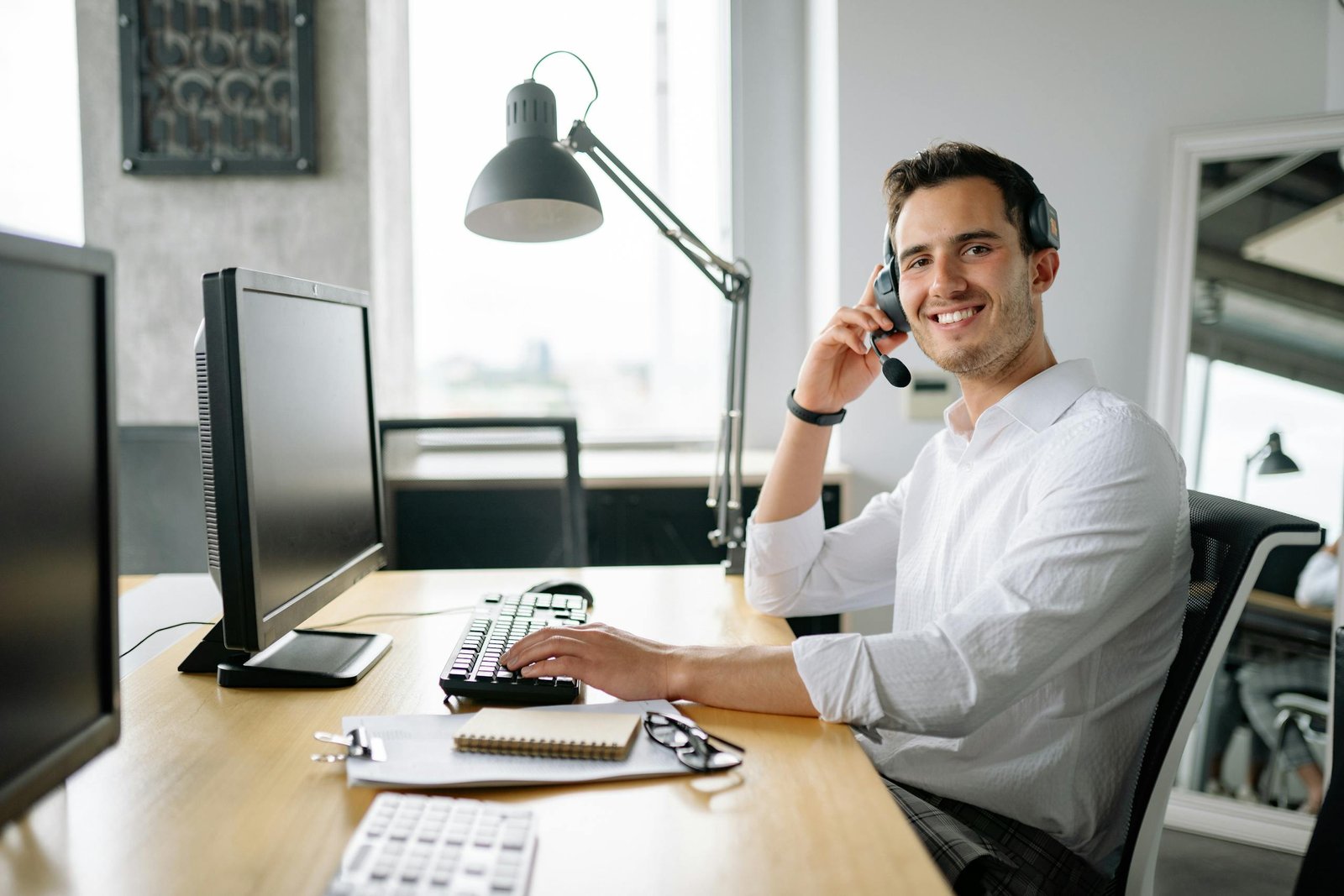 Smiling call center agent working at a desk with a headset and computer in a modern office.